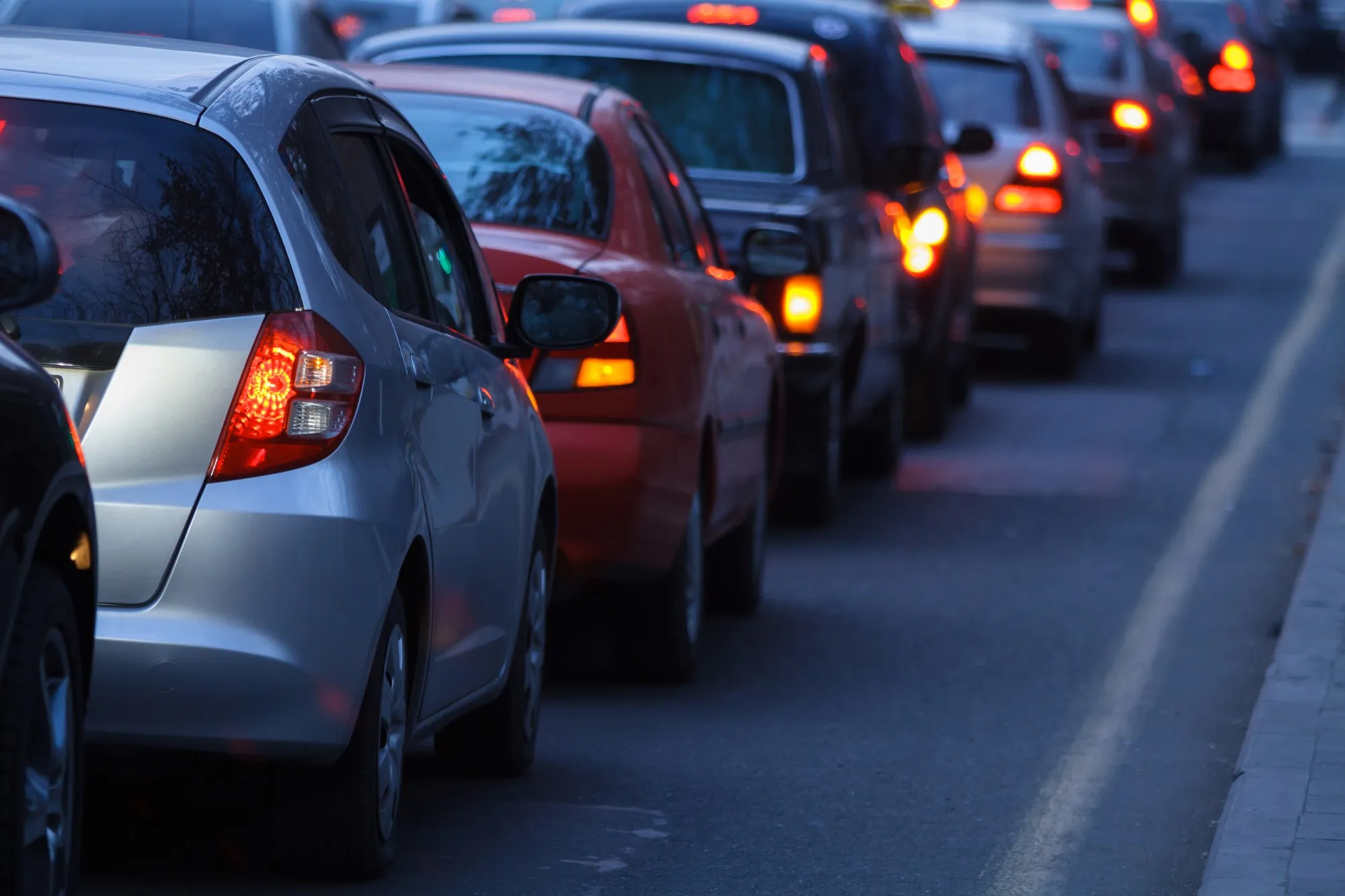 A line of stopped cars with brake lights on at dusk.
